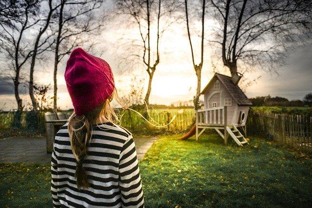 Photo of young girl in a back yard at sunset staring at a very fancy tree house