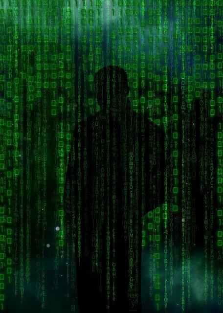 The shadow of a man can barely be made out behind a cascade of green computer coding language.