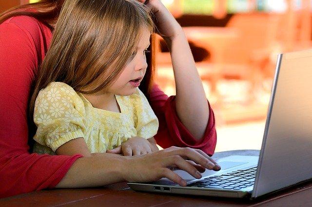 photo of little girl in her mom's lap in front of the laptop